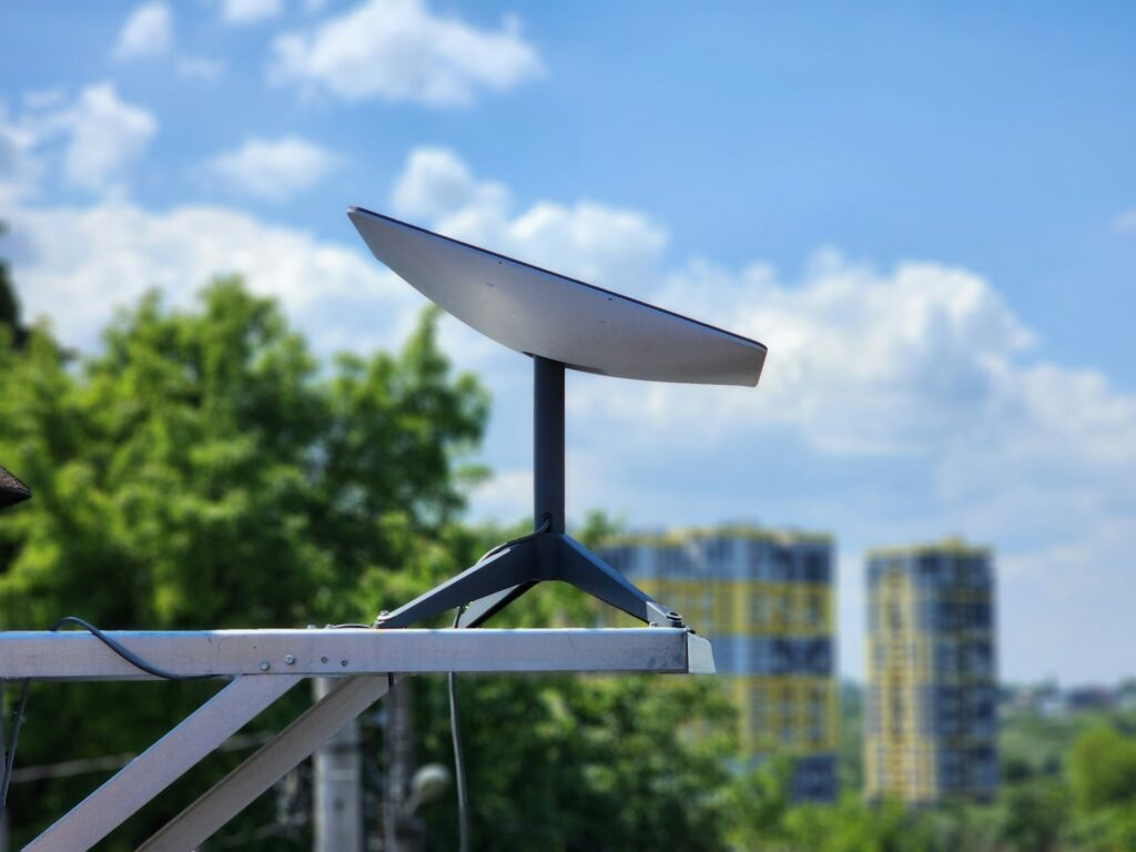 antenna Starlink installata su un supporto in metallo, sullo sfondo una città con un cielo chiaro e delle nuvole